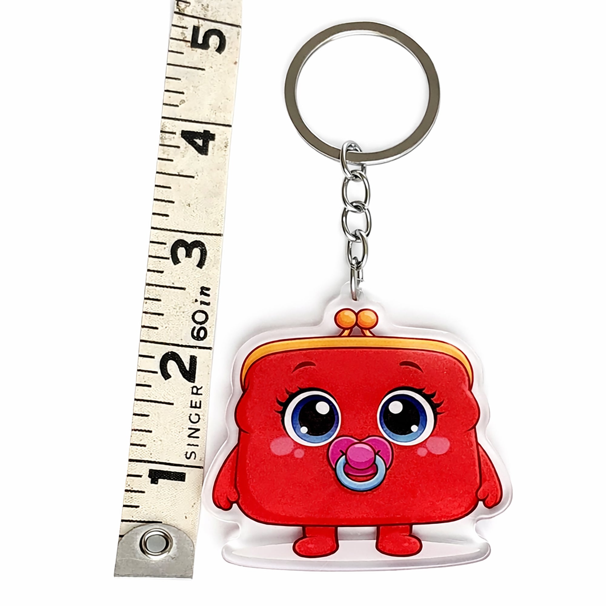Red cartoon character keychain with a pacifier next to a ruler for scale on a white background