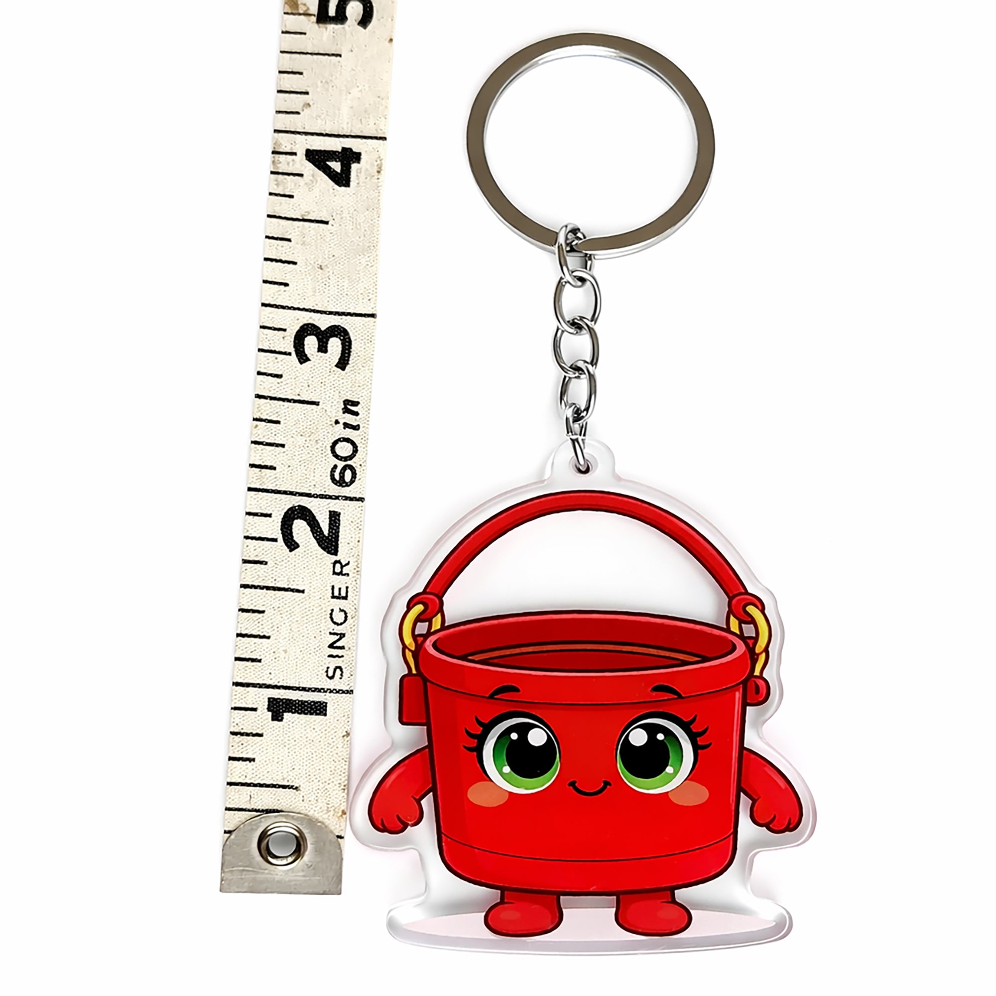 Red bucket keychain with cartoon face next to a ruler for scale on a white background