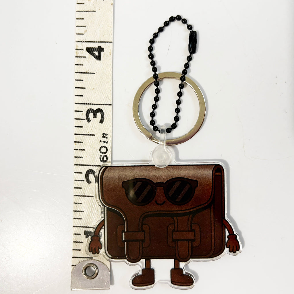 Keychain bag charm with a cartoon purse  and sunglasses design next to a ruler on a white background
