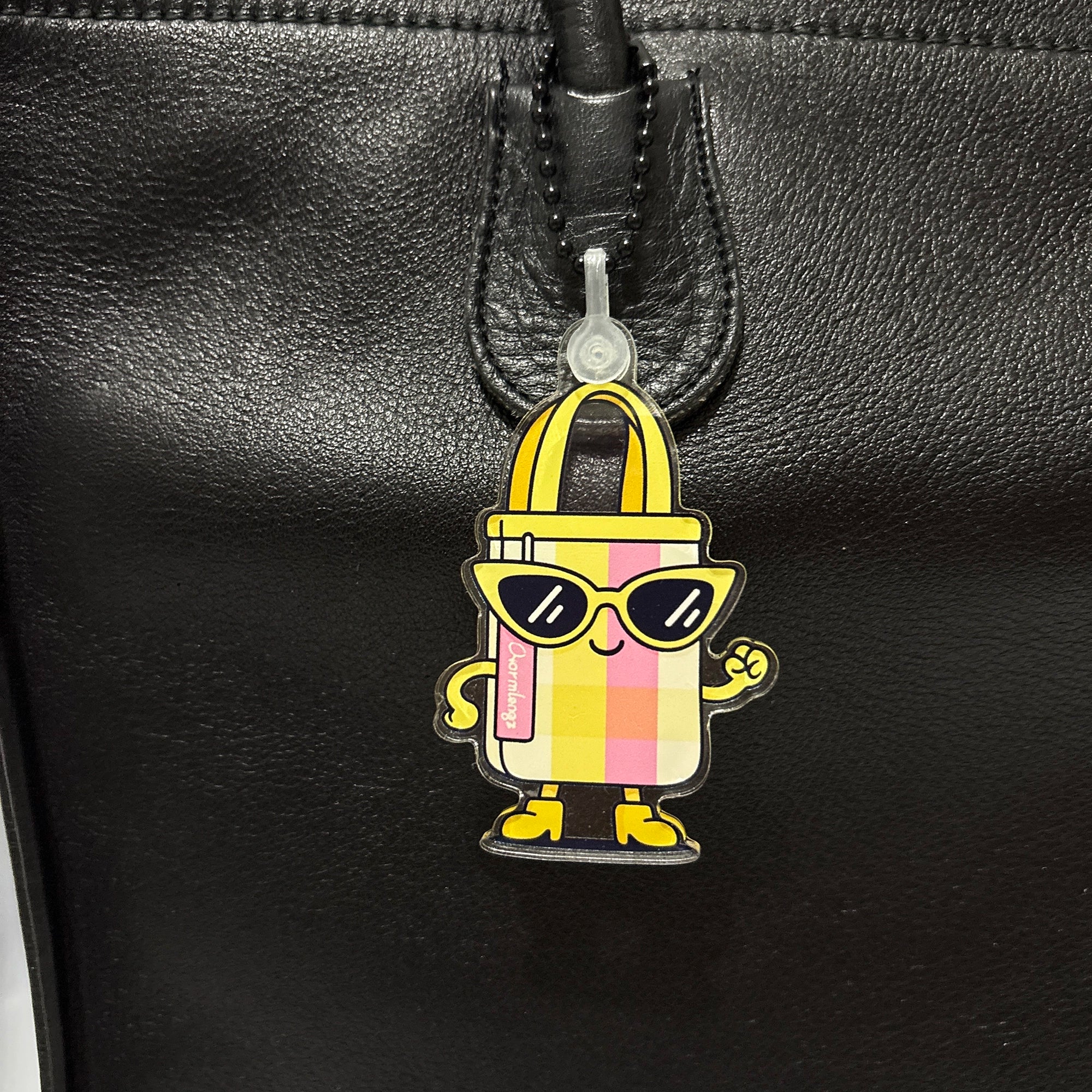 Colorful tote bag shaped bag charm with sunglasses attached to a black leather bag.