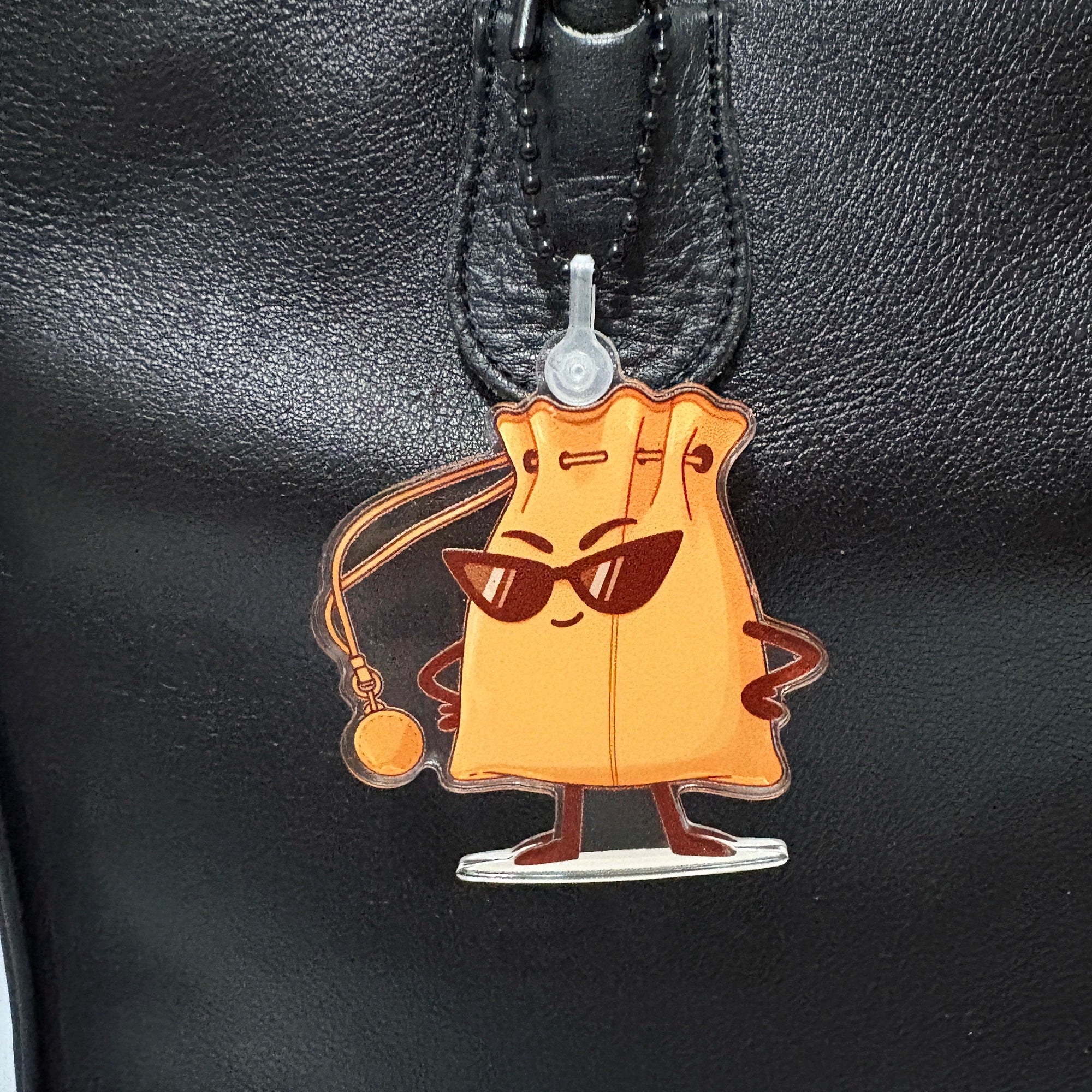 Cartoon character handbag shaped keychain bag charm with sunglasses attached to a black leather bag.
