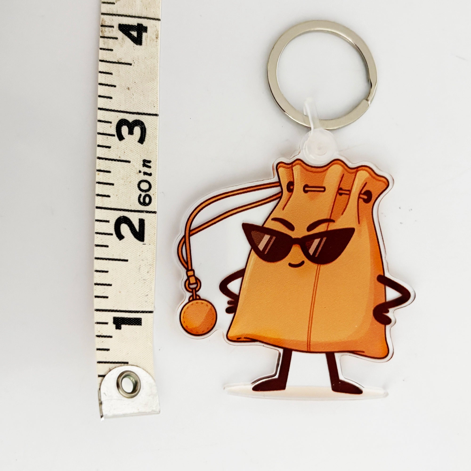 Keychain bag charm with cartoon handbag character  next to a ruler for scale on a white background