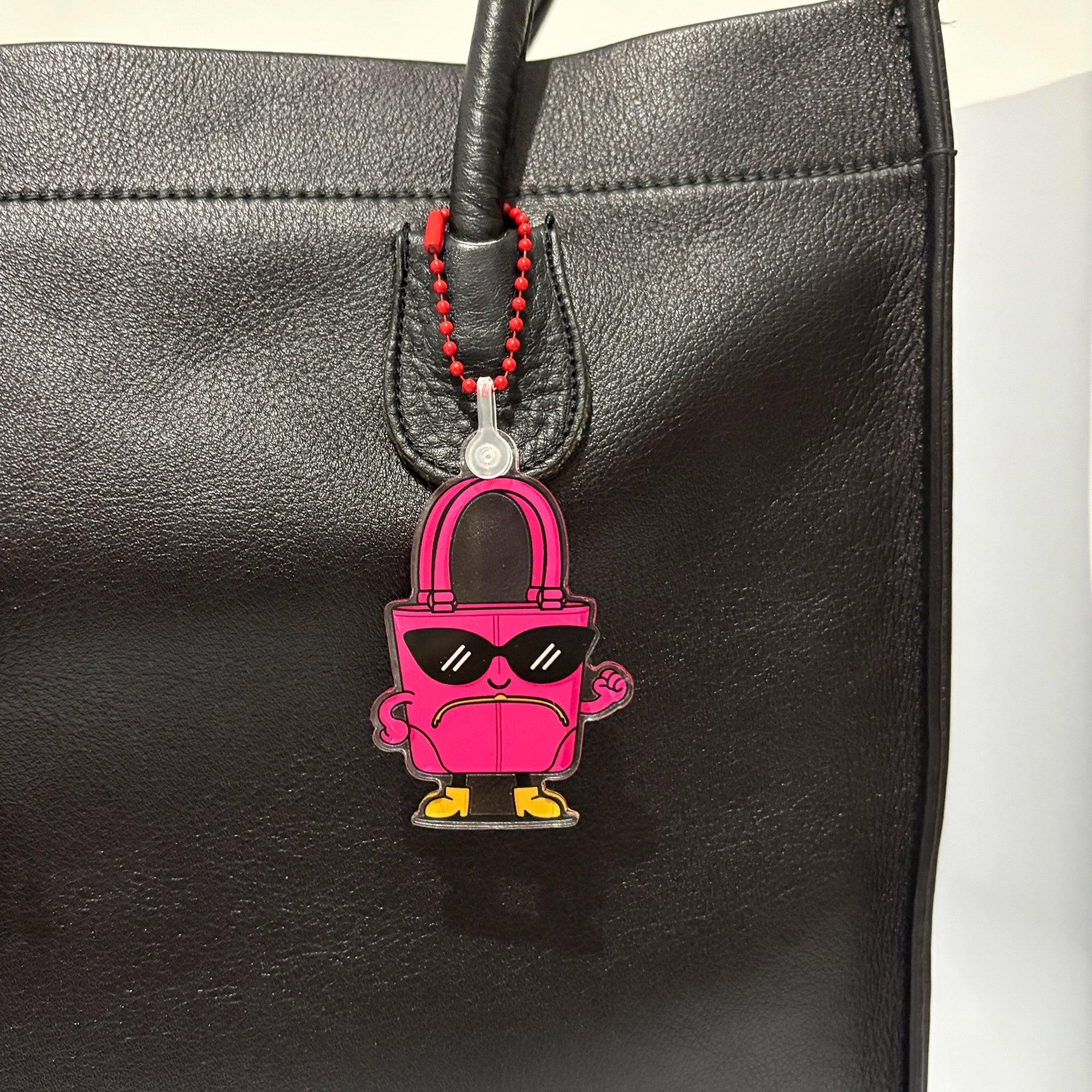Pink lock-shaped keychain bag charm with sunglasses on a black leather bag.