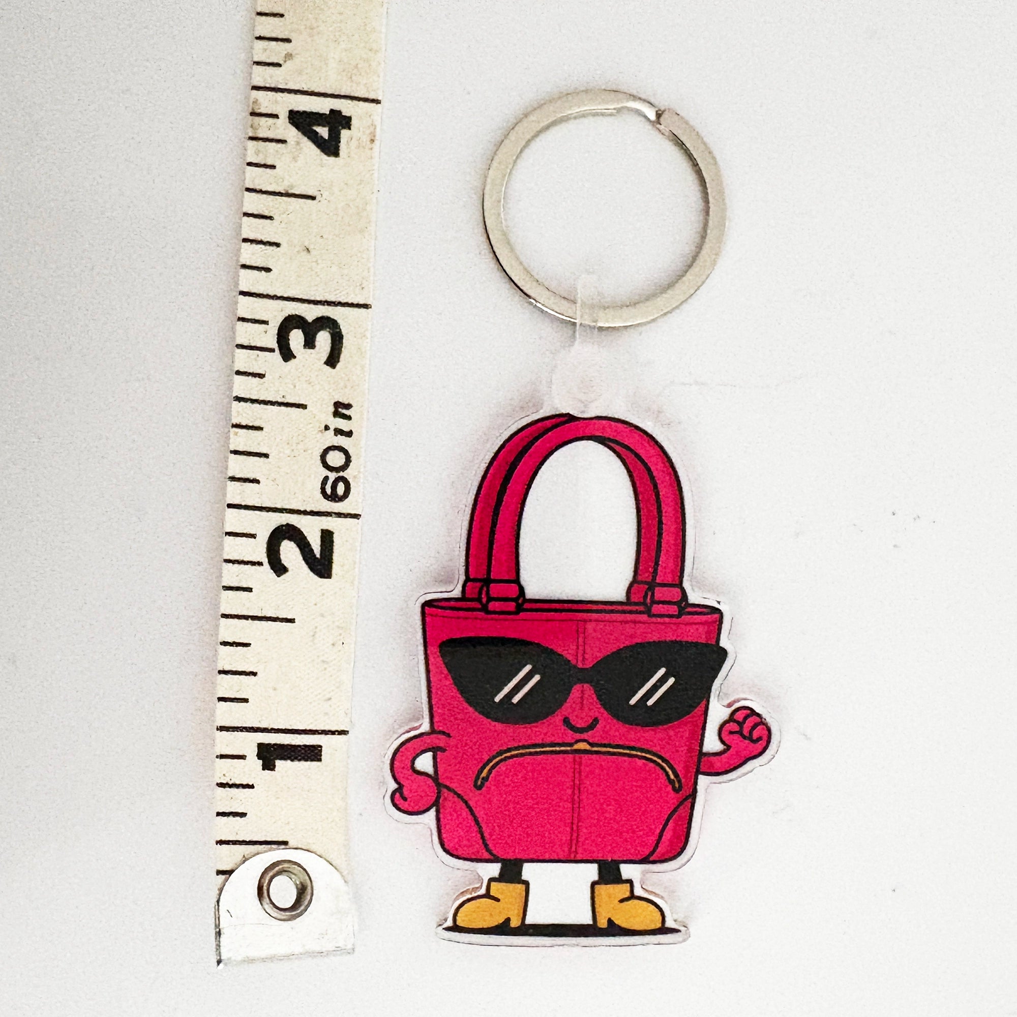 Keychain bag charm shaped like a pink handbag with sunglasses and boots, next to a ruler for scale.