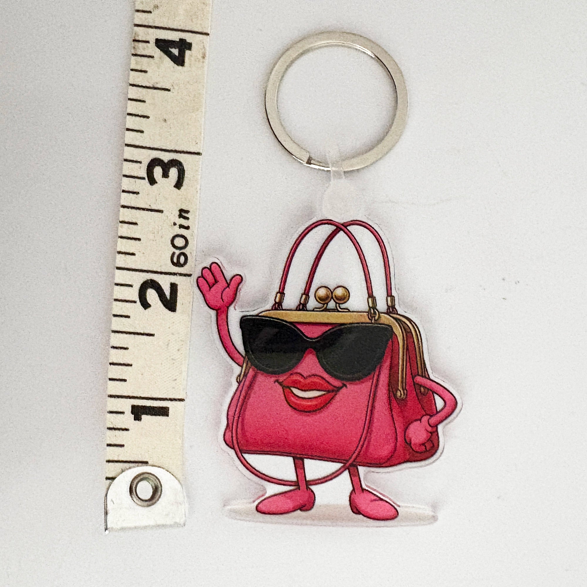 Keychain charm shaped like a pink handbag with sunglasses and shoes, next to a ruler for scale.
