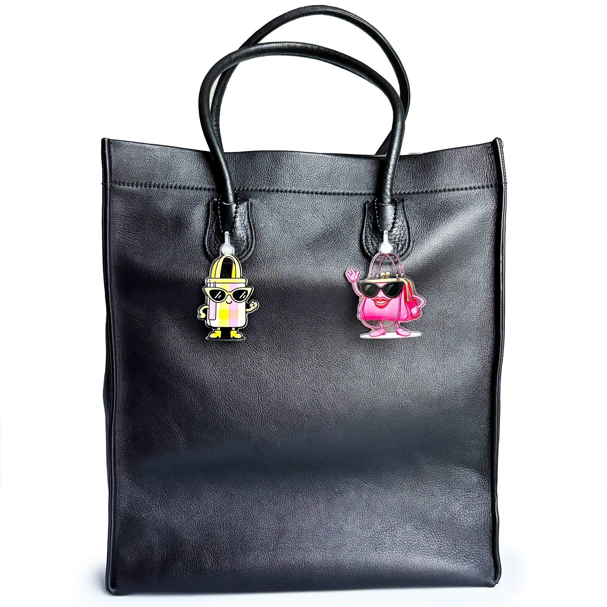 Black leather tote bag with two colorful handbag shaped charms on a white background