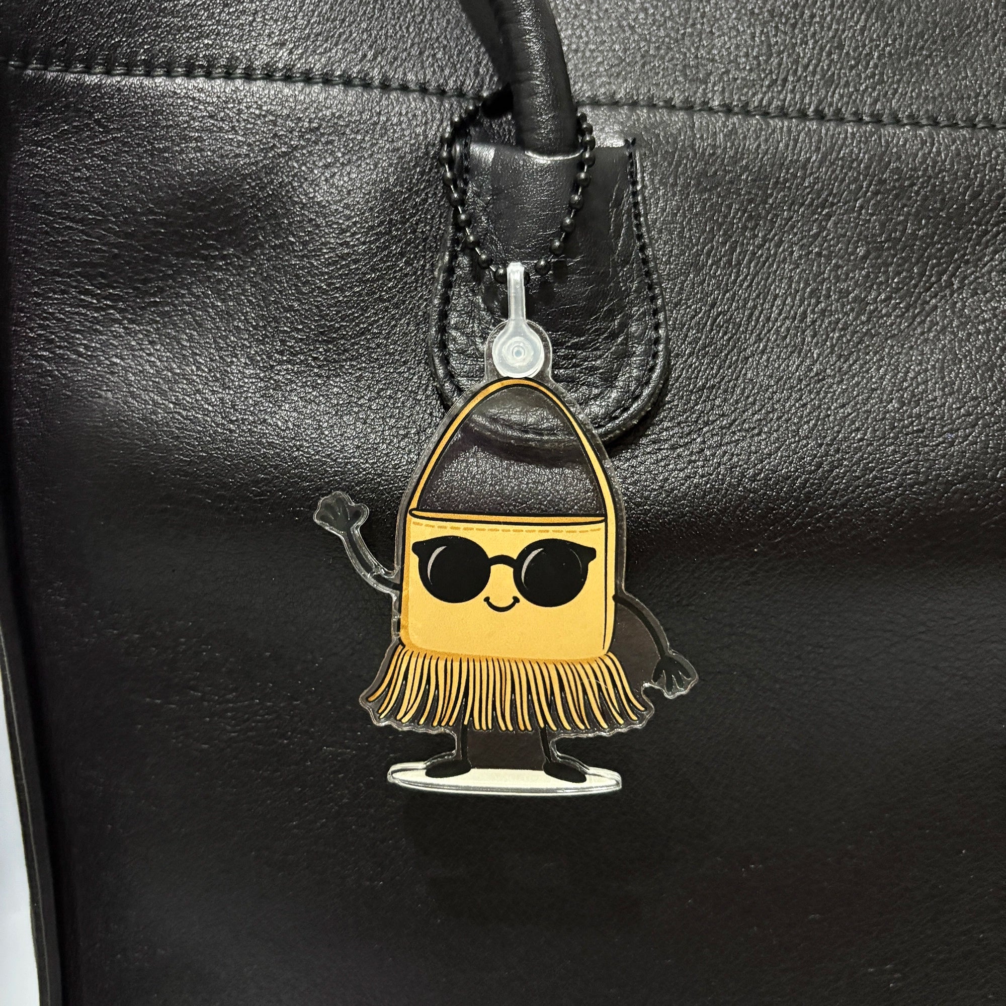 tan handbag-shaped keychain bag charm with sunglasses on a black leather bag.