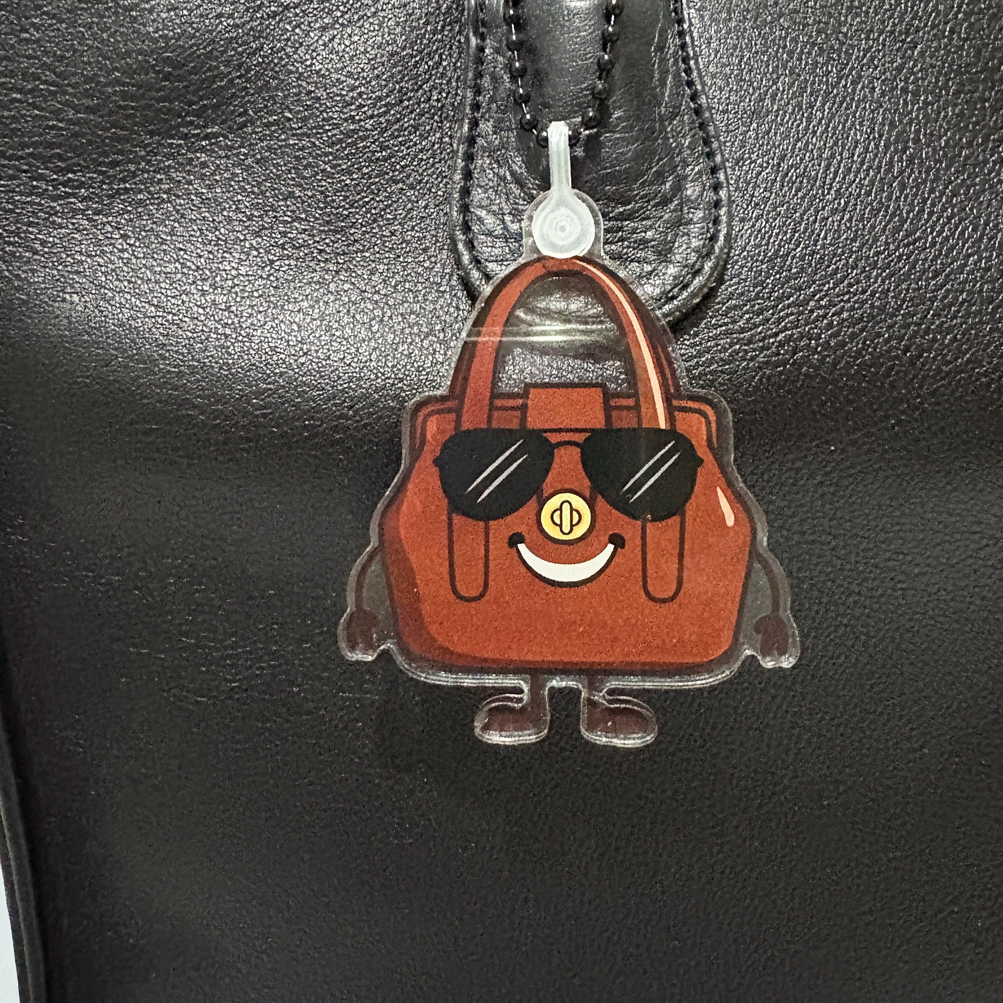 Brown bag-shaped keychain with sunglasses on a black leather surface