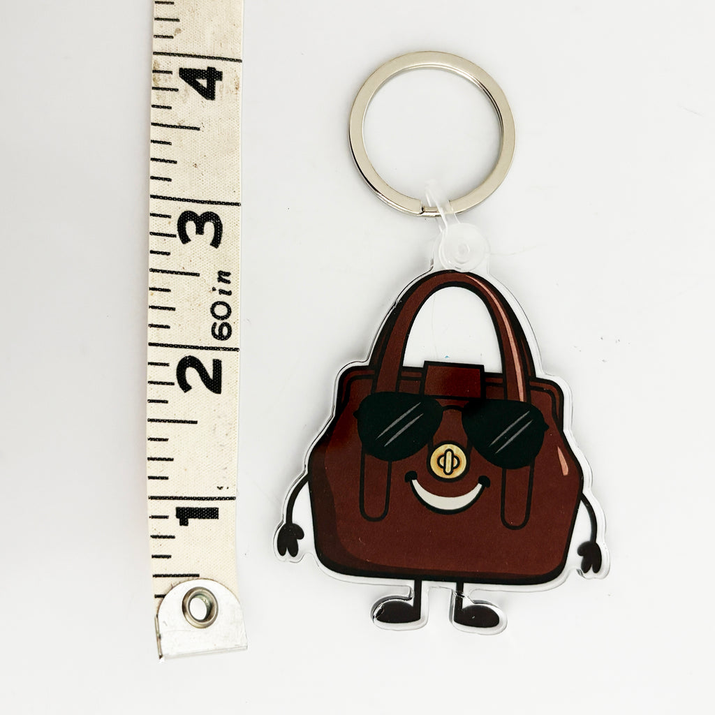 Keychain bag charm shaped like a brown vintage handbag with sunglasses and a gold chain, next to a ruler for scale.