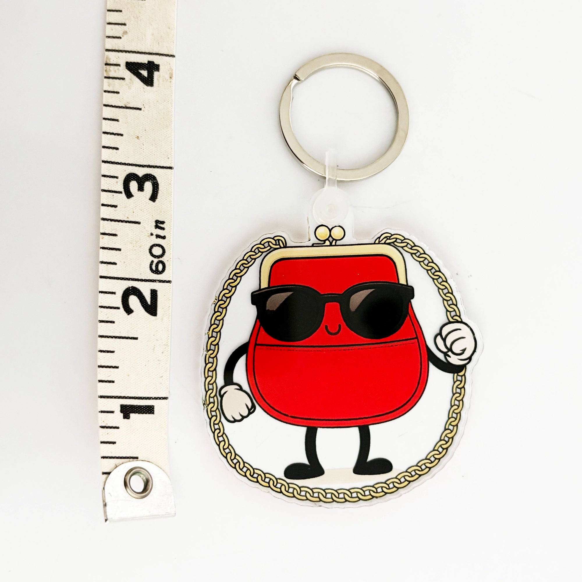 Keychain bag charm with a cartoon-style red purse character wearing sunglasses, next to a ruler for scale.