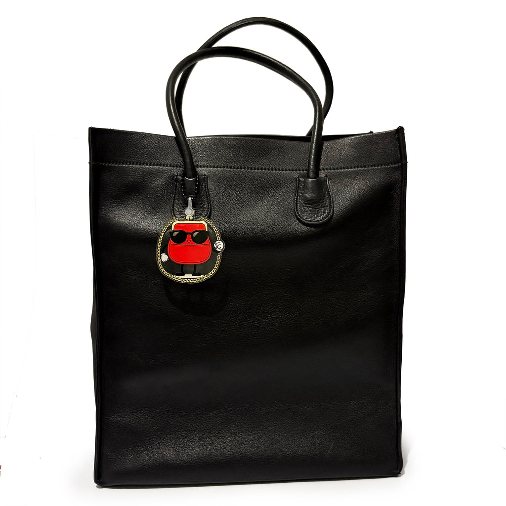 Black tote bag with a red and gold charm on a white background