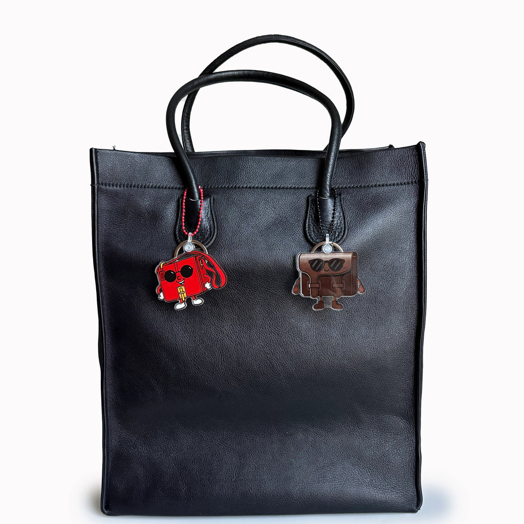 Black tote bag with two colorful charms on a white background