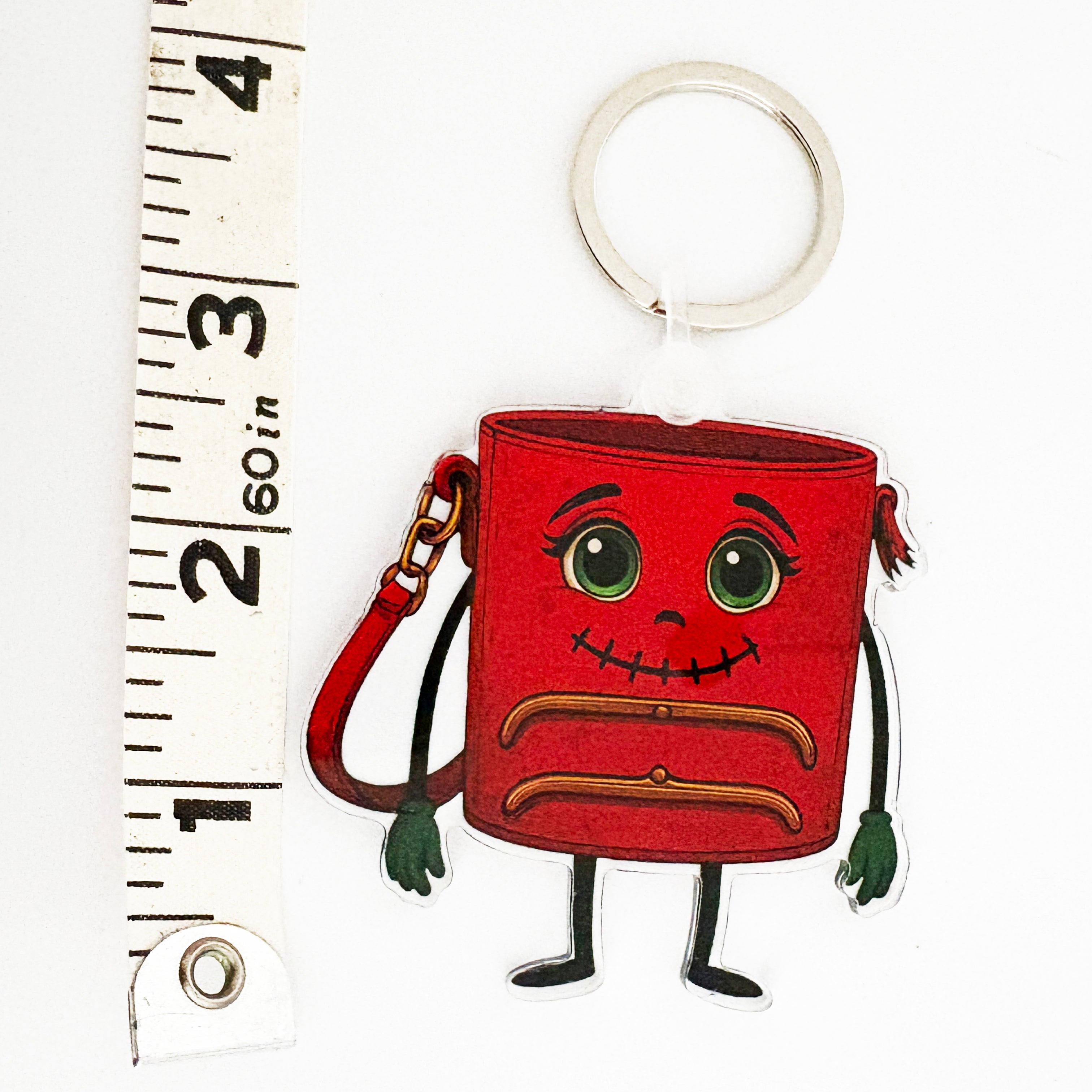 Red ReLuvable TriFramea bag charm keychain with cartoon face next to a ruler on a white background