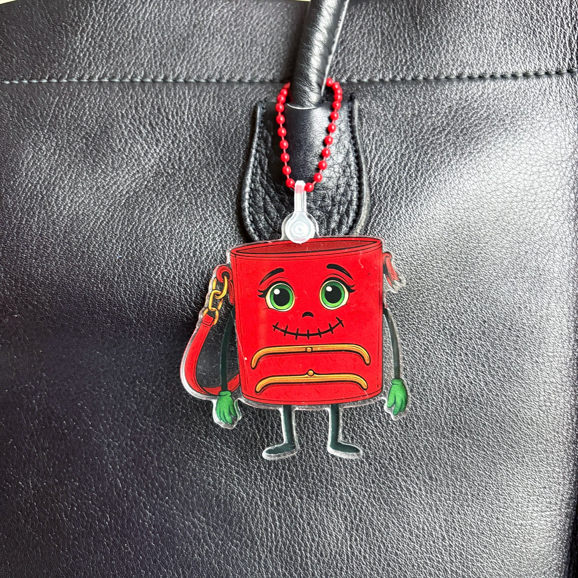 Red ReLuvable TriFramea Bag charm keychain with a face on a black vintage leather surface, close up